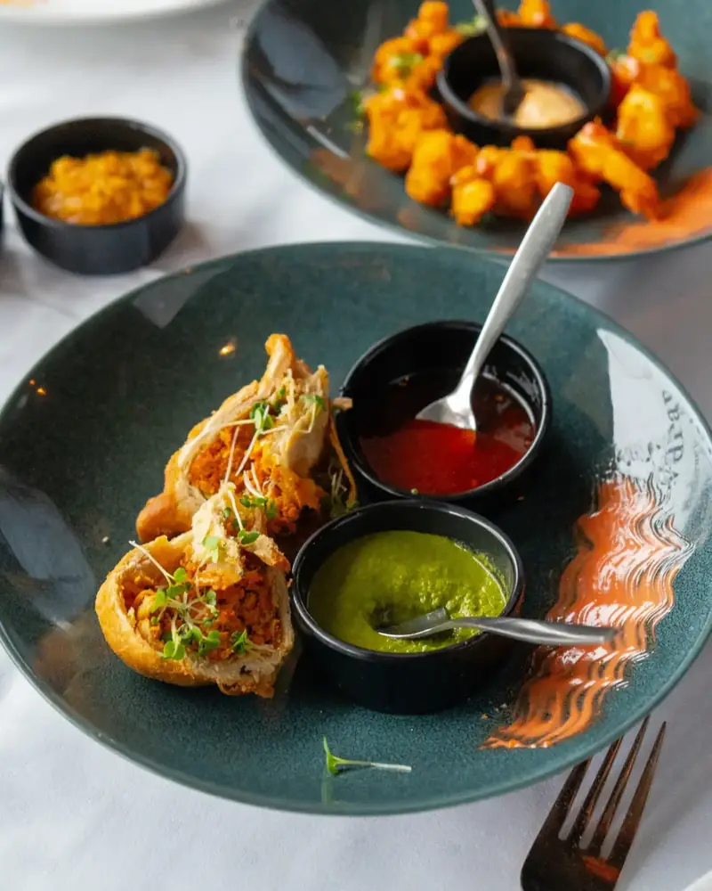 Samosa servert med grønn og rød dipsaus på turkis tallerken